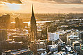 Key visual of the RECHARGE WindPower Summit. View of Hamburg with St. Michael's Church, the Elbphilharmonie, the Port of Hamburg, and City Hall. Wind turbines can be seen in the background.