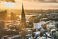 Key visual of the RECHARGE WindPower Summit. View of Hamburg with St. Michael's Church, the Elbphilharmonie, the Port of Hamburg, and City Hall. Wind turbines can be seen in the background.